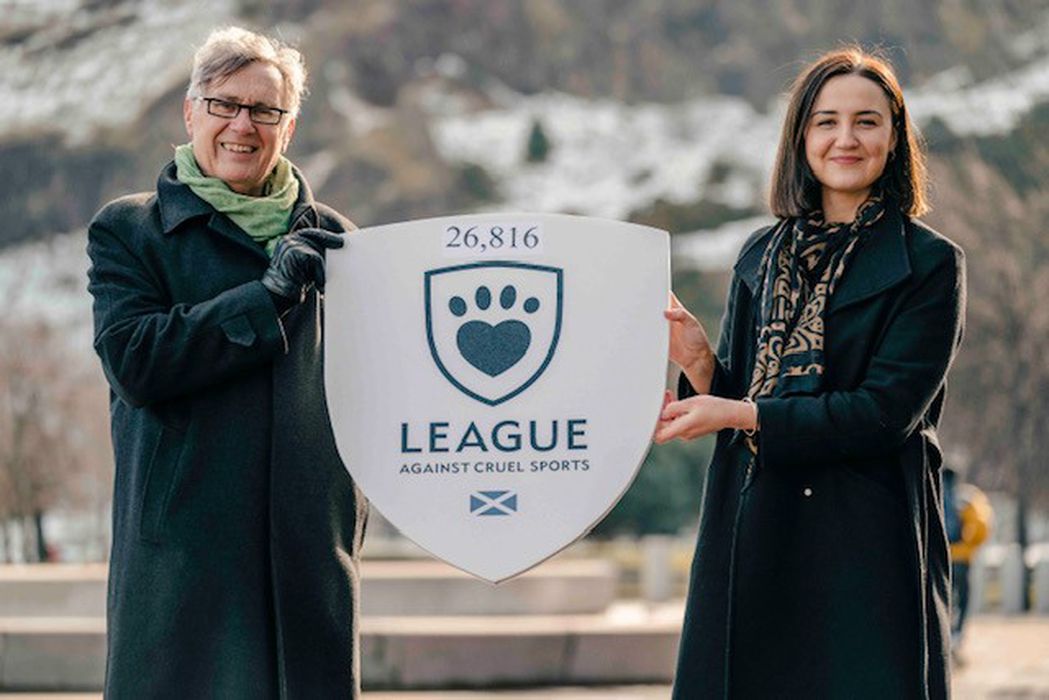 Two people with a sign with the League logo and the number 26816